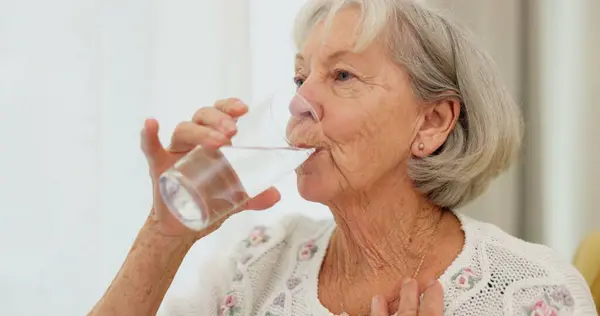 Health, thirsty and mature woman drinking water for hydration and liquid diet detox at home. Wellness, fresh and calm elderly female person enjoying glass of cold drink in modern retirement house