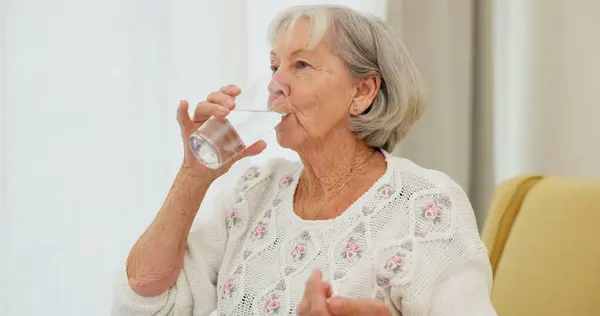 Water, pills and senior woman on a sofa with medicine for health, balance and aging wellness in her home. Tablet, swallow and elderly lady in living room with vitamin c, collagen or iron and calcium.