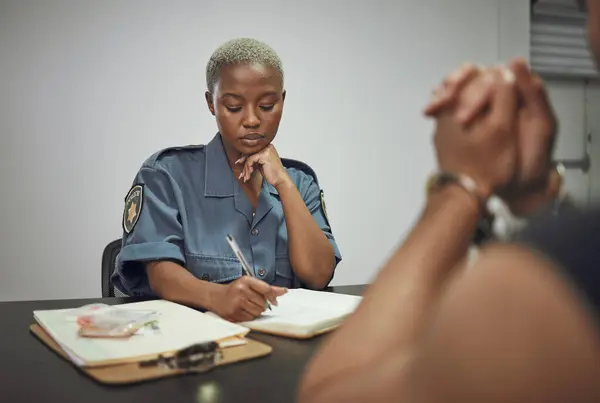 Security, criminal and female police officer at the station writing a legal report for social justice. Law enforcement, crime and male thief in handcuffs talking to woman guard in interrogation room