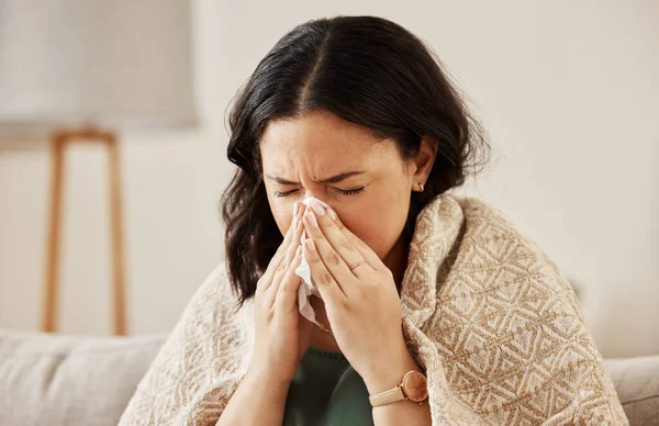 Nose, tissue and sick woman sneezing on a sofa with allergy, cold or flu in her home. Hay fever, allergy and female with viral infection, problem or health crisis in a living room with congestion.
