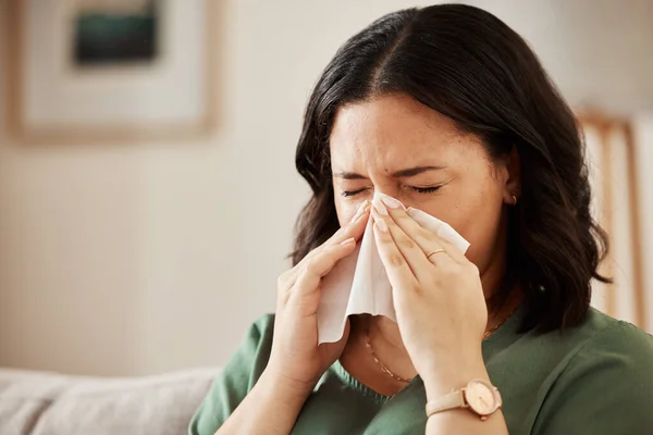 Tissue, blowing nose and woman in a living room with flu, cold and hay fever, crisis or viral infection in her home. Sneezing, allergies and person with health risk in a lounge or coughing illness.