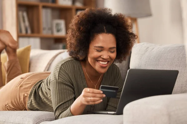 Black woman, credit card and laptop on sofa for online shopping, digital payment and fintech account. Happy female person, computer banking and money for sales, password and ecommerce finance at home.