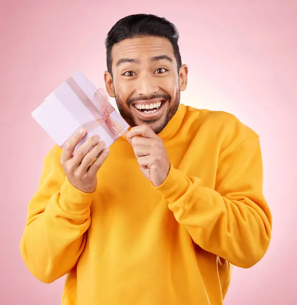 Young man, gift box and studio portrait with excited smile, ribbon and open for celebration by pink background. Asian gen z student, present or prize for giveaway, competition or package for party.