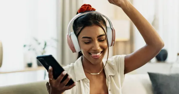 Smartphone, music and happy woman dance on sofa in home, celebration and listening to audio app. Phone, excited Indian person on headphones and radio, sound or freedom in living room on mobile tech.