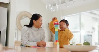 Kaynaşma, gülümseme ve anne çocuğuyla evde çocuk gelişimi için mutfakta yapı taşlarıyla oynuyorlar. Mutlu, sevgi dolu ve genç Asyalı anne evde eğlenmek için kızına tahta oyuncaklarla yardım ediyor.