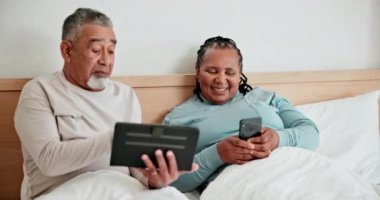 Akıllı telefon, tablet ve yatakta yaşlı çift sabahları yazışıyor ve konuşuyorlar. Teknoloji, mutlu adam ve ırklar arası kadın yatak odasında internet, sosyal medya ve evde online alışveriş.