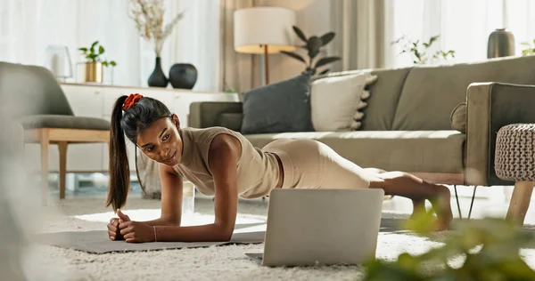 Indian woman, laptop and plank exercise in home for strong fitness, virtual workout or balance. Computer, online challenge and push up on elbow for muscle, power or action on floor in lounge.