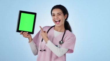 Tablet, yeşil ekran ve bir stüdyoda çalışan kadın hemşire reklam ve pazarlama için bir model alanı işaret ediyor. Dijital teknoloji, kroma anahtarı ve mavi arka planda çalışan kadın sağlık görevlisinin portresi.