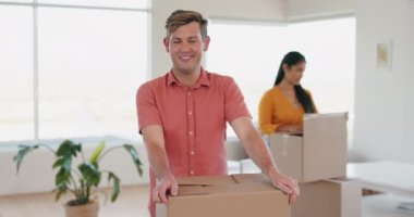 Kutular, paketler ve yeni evine taşınan bir adamın yüzü eşiyle oturma odasına yerleşiyor. Mutlu, gülümse ve evi, evi ya da dairesi için kartonla genç bir erkeğin portresi.