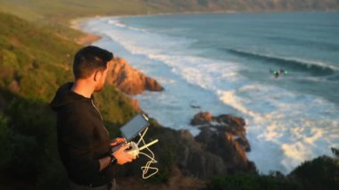 Deniz, teknoloji ve yaz boyunca video görüntüleri için okyanus üzerinde insansız hava aracı uçuran bir adam. Kumsal, dalgalar ve deniz kıyısındaki bir robotu uzaktan kumandayla kontrol eden biriyle görüntüler..