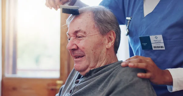 Senior man, nurse and comb hair with smile for grooming, care and wellness with helping hand in retirement. Elderly person, caregiver and haircare in nursing home for support, assisted living or talk.