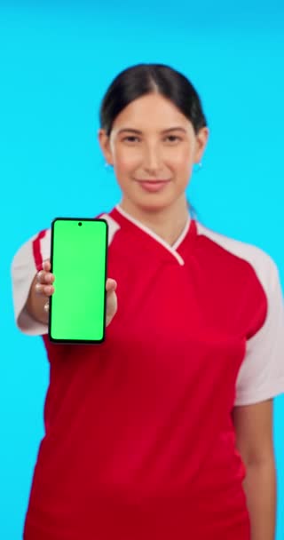 スポーツモックアップ 緑の画面の電話やサッカーの情報やプロモーションを持つ女性 青い背景に空白のモバイルでサッカー選手のアプリ スポーツや顔の肖像画を表示します — ストック動画