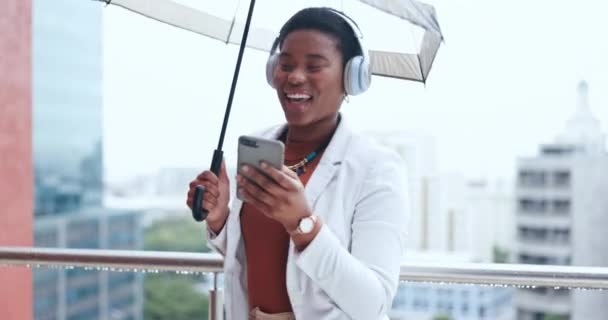 都市部のストリーミングソング オーディオ ラジオのための携帯電話を持つ都市の傘 ヘッドフォン ビジネス女性 オフィス 建物のためのバルコニーで雨 企業の労働者および女性のダンス — ストック動画