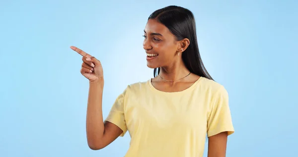 Woman, pointing and deal with marketing, information and direction for announcement in studio. Blue background, person and promotion with smile and sale with offer and show hand sign of student.