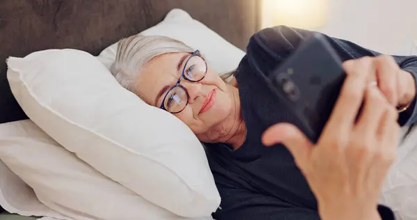 Cellphone, relax and senior woman in bed networking on social media, mobile app or internet. Technology, rest and elderly female person in retirement scroll on website with phone in bedroom at home