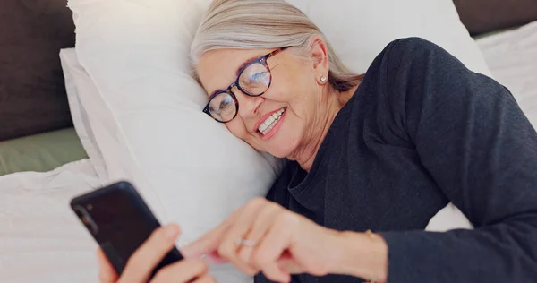 Happy, senior woman and reading with phone in bed or streaming funny, comedy or meme on social media. Elderly person, smile or relax with cellphone at night in bedroom with communication or chat.
