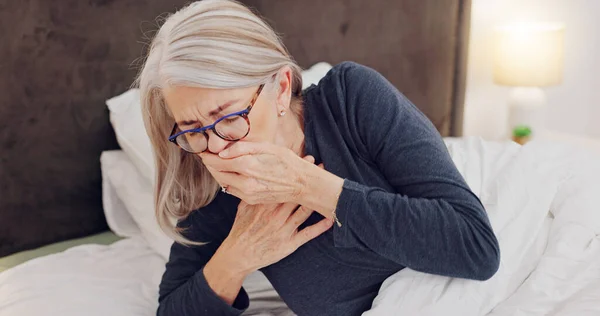 Illness, cough and senior woman in bed with allergies, flu or cold on a weekend morning at home. Sick, chest pain and elderly female person in retirement with asthma or infection in bedroom at house