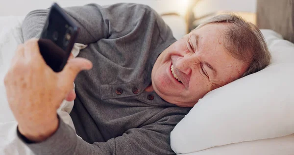 Happy, senior man and reading with phone in bedroom or streaming funny, comedy or meme on social media. Elderly person, smile or relax with cellphone at night in bed with communication or online chat.