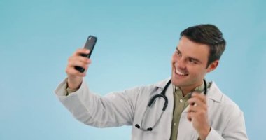 Selfie, steteskoplu mutlu adam ve doktor stüdyodaki resim ve barış tabelasına bakıyor. Fotoğraf, tıbbi profesyonel gülümseme ve mavi arka planda izole edilmiş tele sağlık için el hareketi