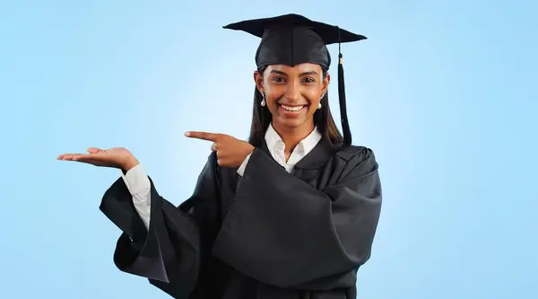 Graduation, portrait and happy woman point, palm gesture and advertising learning, university info or college study. Studio mockup space, student commercial ads or school graduate on blue background.