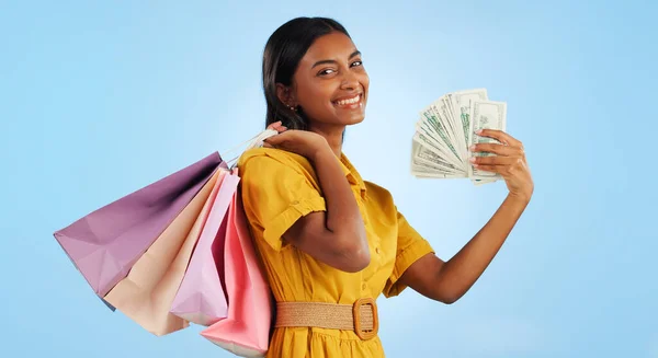 Woman, shopping bag and cash fan, wealth and commerce with customer in portrait on blue background. Money, financial freedom and retail, fashion and product choice, rich and store discount in studio.
