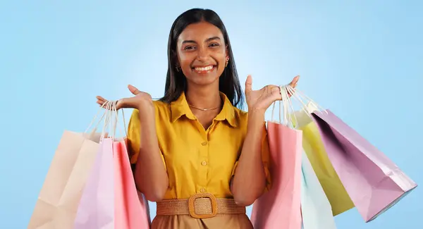 Happy woman, smile and hand with shopping bags in studio for mock up in retail, marketing or promotion on blue background. Indian person, shopaholic and portrait in offer in fashion, cosmetic or sale.