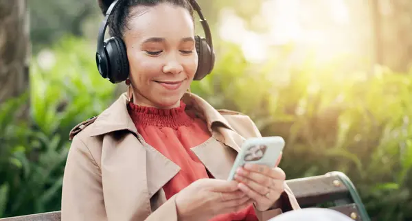 Smile, phone and woman with headphones for streaming radio, playlist and podcast or relax in outdoors. Happy female person, listening to song, sound and music or audio, nature and internet on mobile.