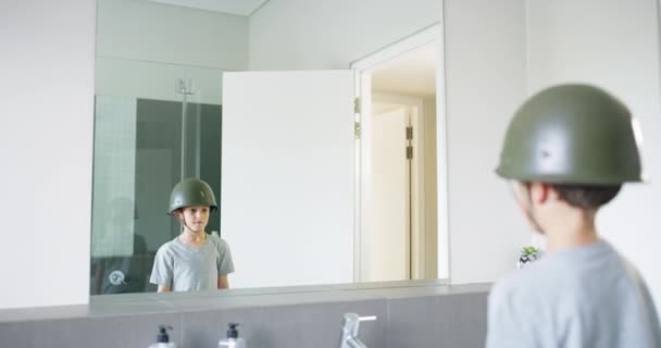 家庭でヘルメットを持った子供 ファンタジーのドレスアップでバスルームで鏡に敬礼 軍のヒーロー 夢と想像 軍のゲームコスプレでトイレの反射で考える少年 — ストック動画
