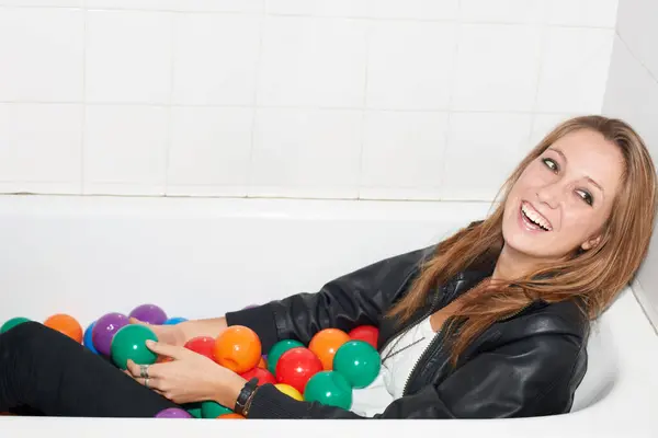 ファッション スタイル 家庭でのトレンディなヒップスターの笑顔のためのバスタブでボール 面白いと女性 浴室にボディが付いている色 球またはプラスチックが付いている浴槽の笑う人 カナダのリラックスして涼しい服 — ストック写真