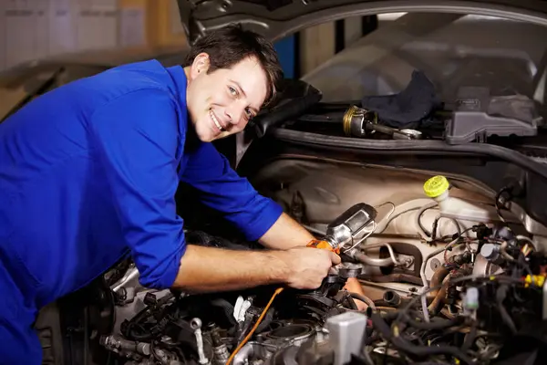 Portrait, smile and car with a mechanic man in a workshop as an engineer looking at the engine of a vehicle. Garage, service or repair with a happy technician working under the hood of an automobile.