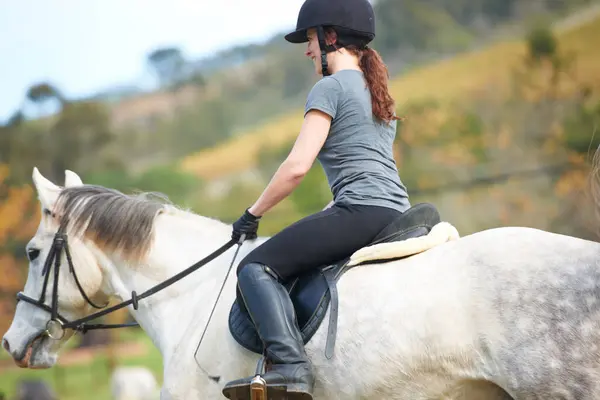 Horse riding, back or woman in countryside outdoor with rider or jockey for recreation or wellness. Sports, ready or equestrian with a healthy animal to start training, exercise or workout on farrm.