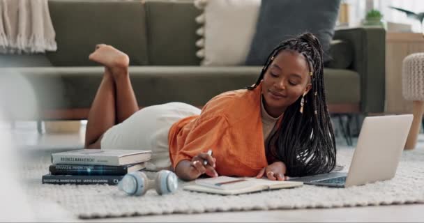 ラップトップ 女性はモダンなアパートのリビングルームの床にノートを書いています テクノロジー 若いアフリカの女性が自宅のラウンジでコンピュータで大学を学ぶ — ストック動画