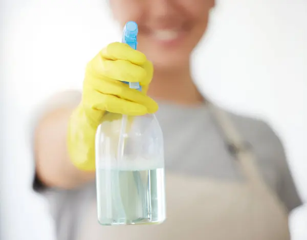 One unrecognizable woman holding a cleaning product while cleaning her apartment. An unknown domestic cleaner wearing latex cleaning gloves.