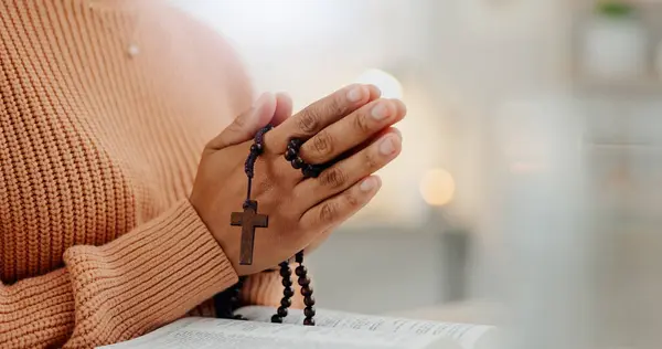Closeup hands, rosary and a bible for prayer, spiritual support and hope from Jesus. House, God and a person with a cross and book for help, trust and gratitude as a Christian for the gospel.