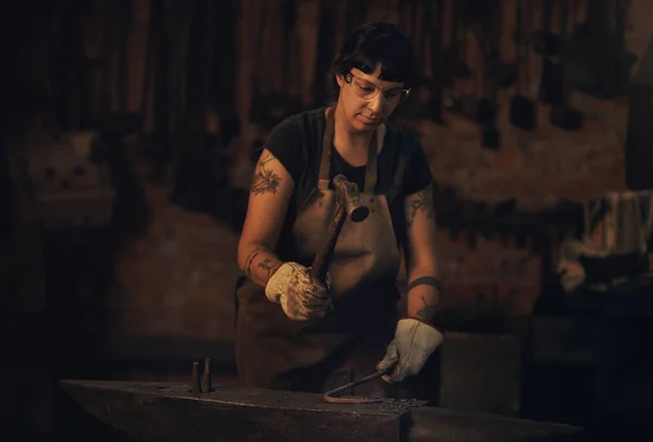 Hard work is always the way. a young woman hitting a hot metal rod with a hammer in a foundry