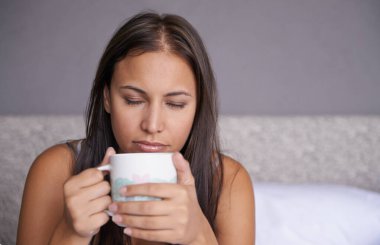 Hiçbir şey onu bir fincan kahveden daha fazla rahatlatamaz. Genç bir kadın sıcak bir içecekle yatağında dinleniyor.