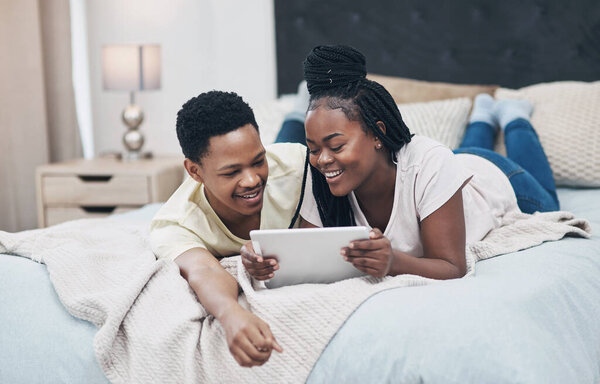 Dates can be just as fun during lockdown. a young couple using a digital tablet while relaxing on their bed at home