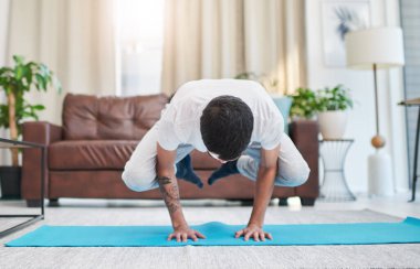 Yoga beni zihinsel ve fiziksel olarak dönüştürdü. Evindeki oturma odasında yoga yapan yakışıklı bir genç adam.