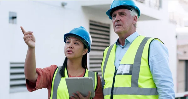 Construction, team and tablet for inspection with people at job site, mentor and apprentice with communication. Architecture, engineering and digital floor plan, old man and woman outdoor in meeting.