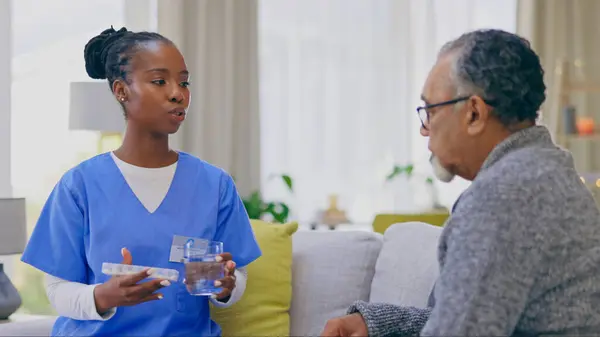 Assisted living, healthcare of medicine with an old man and nurse in a home for medical care or treatment. Help, pills or chronic medication with a black woman volunteer talking to a senior patient.