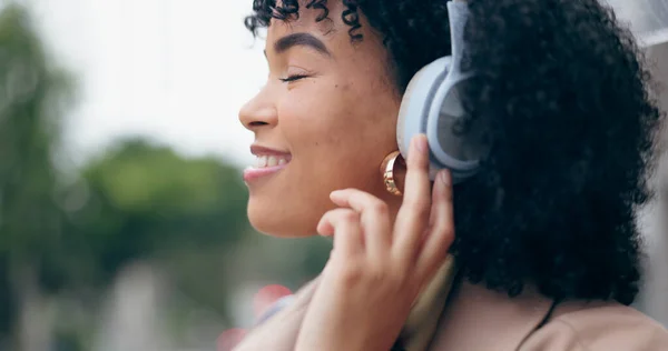 Businesswoman, headphones and listening to music with eyes closed on street, city or outside by commute. African person, curly hair and smile for podcast, streaming or radio with internet, web or app.