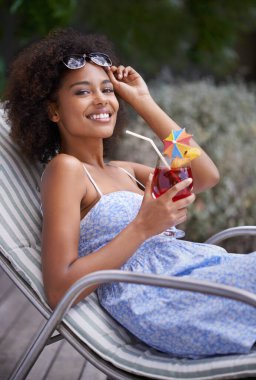 Living life to the max. an attractive ethnic woman holding up her sunglasses with a cocktail outdoors clipart