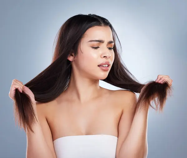 Young mixed race woman holding her long brown hair and looking at damaged split ends. Woman looking upset about hair care problems.
