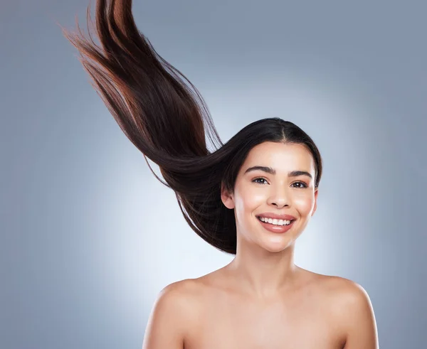 Portrait of a beautiful brunette woman with flawless skin and healthy hair. Young girl with long brown hair flying in the wind against a studio background.