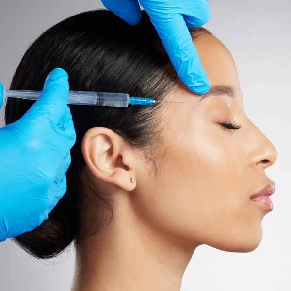 Closeup of a gorgeous mixed race woman getting botox filler. Hispanic model getting filler to reduce wrinkles against a grey copyspace background in a studio.
