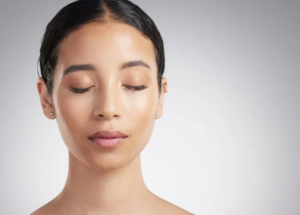 A beautiful young mixed race woman with glowing skin posing against grey copyspace background. Hispanic woman with natural looking eyelash extensions finds inner peace in a studio.