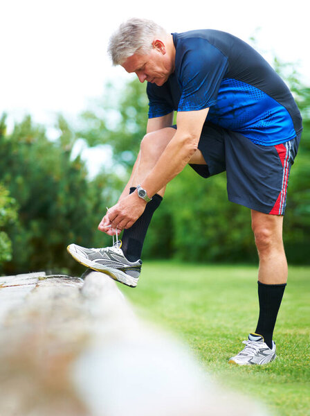 Senior, tie or runner with shoes on rock by nature for exercise, training or outdoor workout. Fitness, healthy man or mature person in park with sports footwear ready for jog, walking or wellness.