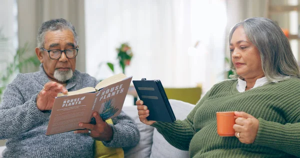 Reading, relax and senior couple on a sofa with book, tablet and coffee while bonding at home together. Literature, ebook and old people chilling with tea in a living room calm and enjoy retirement.