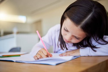 Masada ödev yapan küçük bir kız öğrenci. Not defterine yazan akıllı ilköğretim çocuğu.