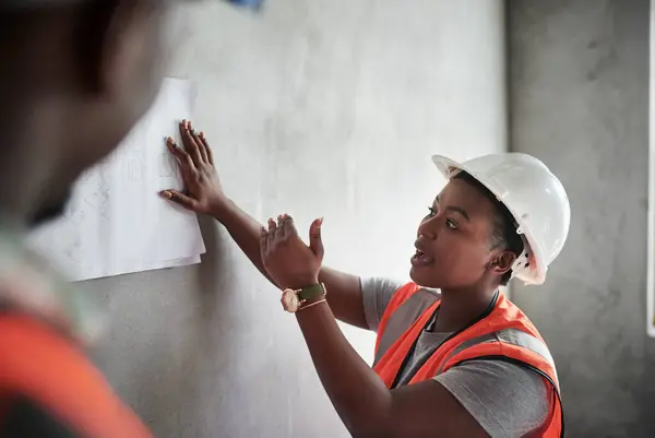 Builders do it without boardrooms. a young man and woman going over building plans at a construction site